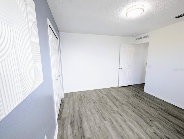 unfurnished bedroom featuring visible vents, a textured ceiling, a closet, and wood finished floors