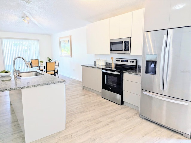 kitchen featuring white cabinetry, light wood-style flooring, appliances with stainless steel finishes, a textured ceiling, and a sink