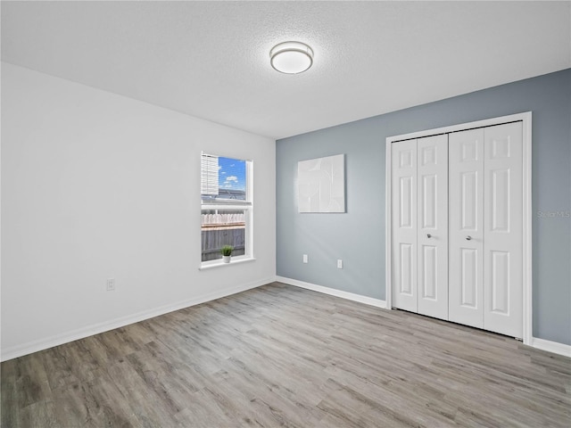 unfurnished bedroom featuring a closet, baseboards, a textured ceiling, and wood finished floors