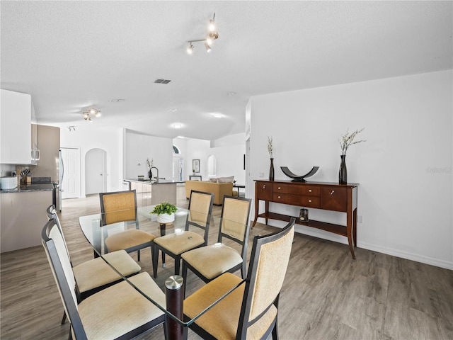 dining room with visible vents, baseboards, arched walkways, a textured ceiling, and light wood-type flooring