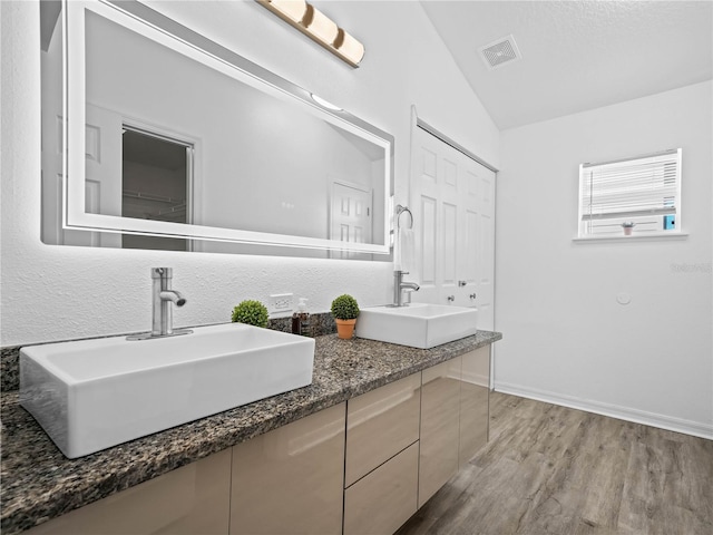 bathroom featuring visible vents, wood finished floors, lofted ceiling, and a sink