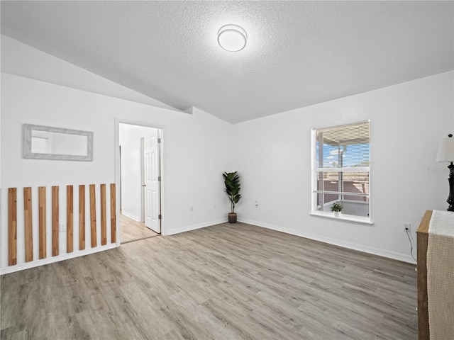 spare room with a textured ceiling, wood finished floors, baseboards, and vaulted ceiling