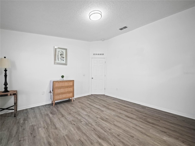 interior space featuring visible vents, a textured ceiling, baseboards, and wood finished floors