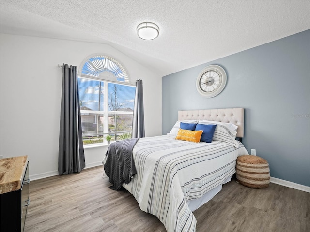 bedroom featuring vaulted ceiling, wood finished floors, baseboards, and a textured ceiling