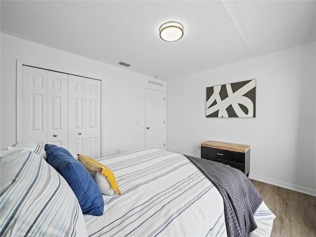 bedroom featuring visible vents, a textured ceiling, wood finished floors, a closet, and baseboards