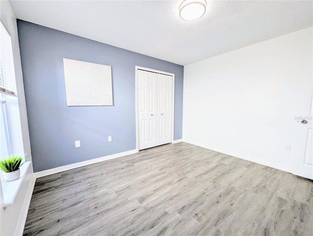 unfurnished bedroom with a closet, a textured ceiling, baseboards, and wood finished floors