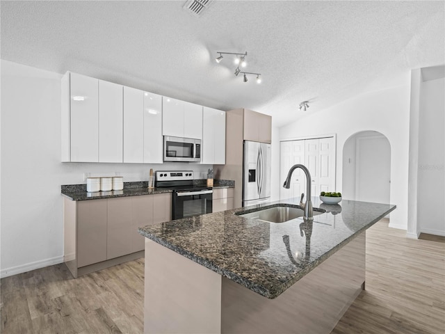 kitchen featuring lofted ceiling, arched walkways, appliances with stainless steel finishes, a textured ceiling, and modern cabinets