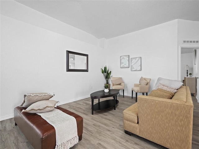 living area featuring lofted ceiling, wood finished floors, visible vents, and baseboards