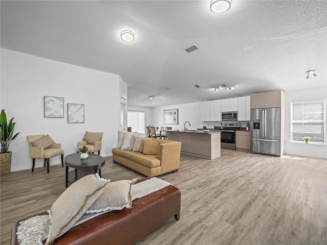 living area featuring light wood-type flooring, visible vents, baseboards, and a textured ceiling