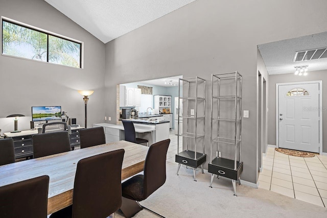 dining room featuring visible vents, light colored carpet, a textured ceiling, and high vaulted ceiling