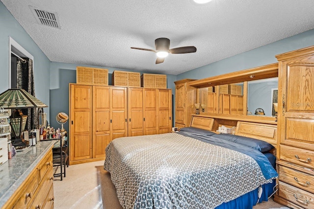 bedroom with visible vents, light colored carpet, a closet, a textured ceiling, and a ceiling fan