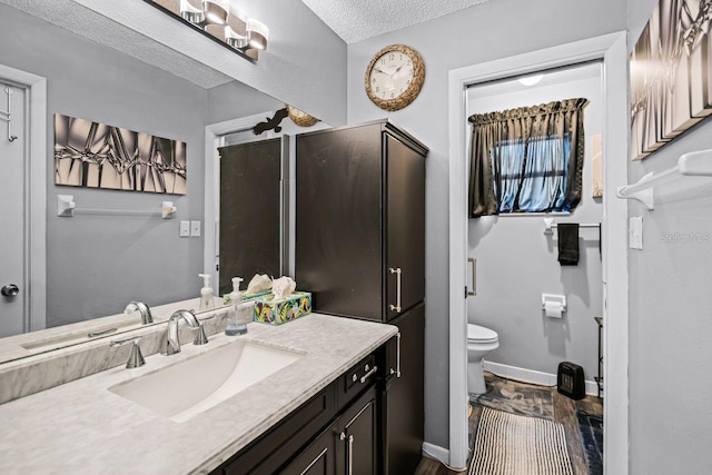 bathroom with baseboards, toilet, vanity, wood finished floors, and a textured ceiling