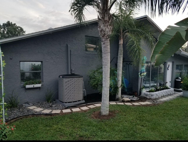 view of property exterior featuring stucco siding, cooling unit, and a yard