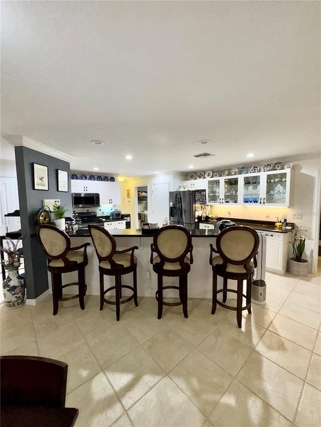 kitchen featuring a breakfast bar, black fridge, stainless steel microwave, dark countertops, and white cabinetry