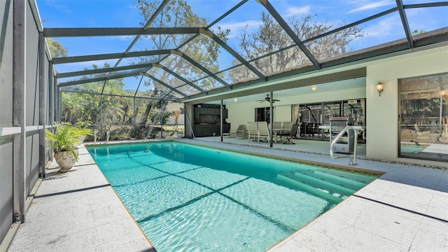 pool with glass enclosure, a patio area, and ceiling fan