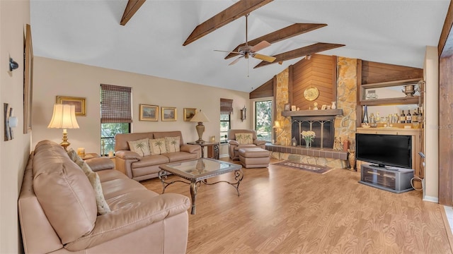 living room featuring beamed ceiling, high vaulted ceiling, wood finished floors, a stone fireplace, and ceiling fan