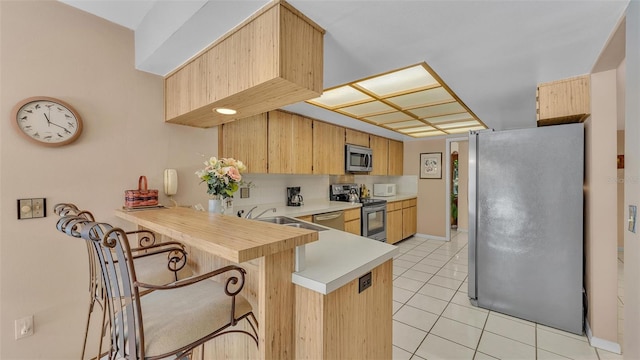 kitchen featuring a sink, appliances with stainless steel finishes, a peninsula, light countertops, and light tile patterned floors