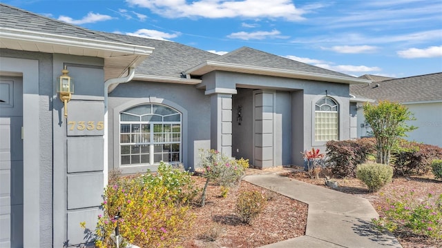 doorway to property with stucco siding and a shingled roof