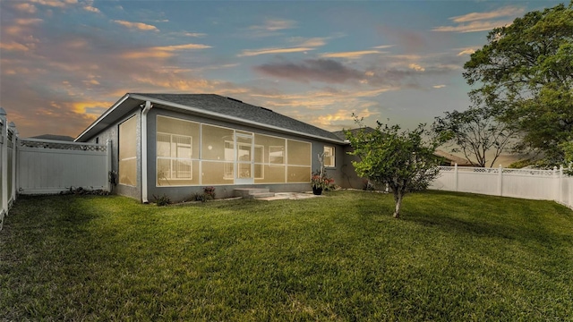 back of property at dusk featuring a sunroom, a lawn, a fenced backyard, and stucco siding