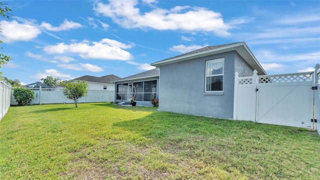 rear view of property featuring a lawn, a sunroom, a fenced backyard, and a gate