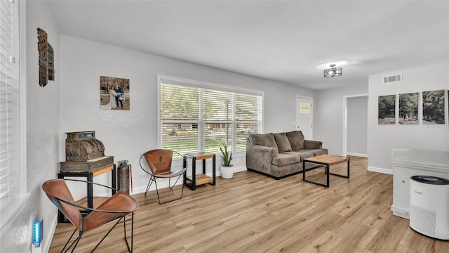 living room with light wood-style floors, visible vents, and baseboards