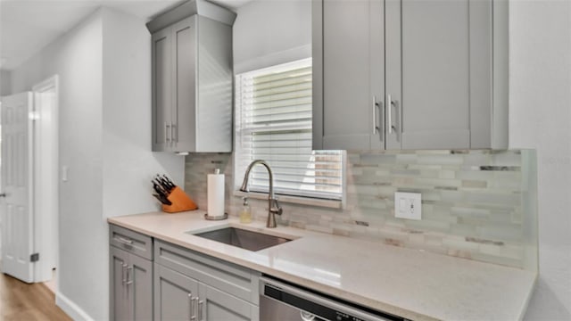 kitchen with a sink, tasteful backsplash, stainless steel dishwasher, and gray cabinetry