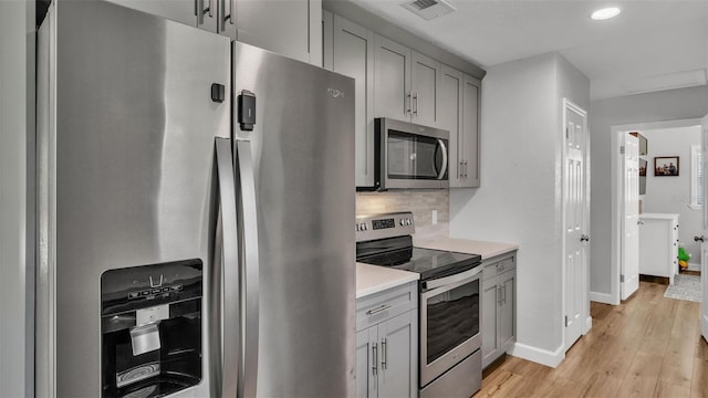 kitchen with backsplash, gray cabinetry, light wood-type flooring, light countertops, and appliances with stainless steel finishes