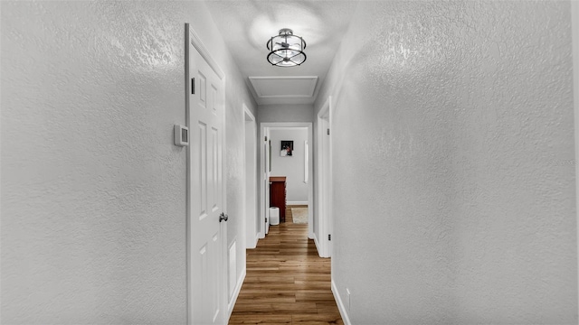 hallway with attic access, wood finished floors, baseboards, and a textured wall