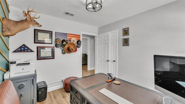 office area with light wood-style flooring, baseboards, visible vents, and a textured ceiling