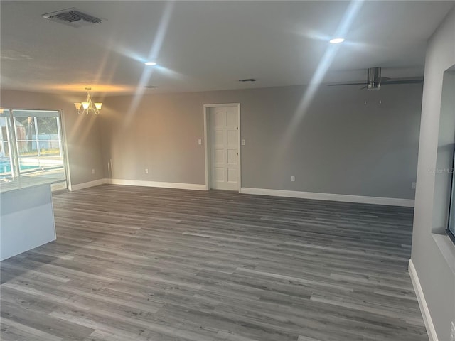 unfurnished room with visible vents, ceiling fan with notable chandelier, baseboards, and wood finished floors