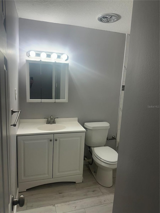 bathroom with a textured ceiling, toilet, vanity, and wood finished floors