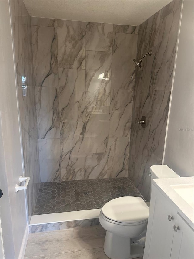 full bathroom with a tile shower, toilet, and vanity