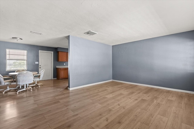 living area featuring light wood-style flooring, baseboards, visible vents, and a textured ceiling