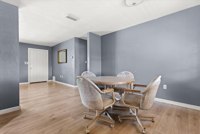 dining space featuring a textured wall, baseboards, and wood finished floors