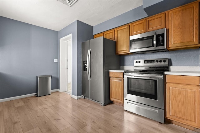 kitchen with baseboards, stainless steel appliances, light countertops, light wood-style floors, and brown cabinets