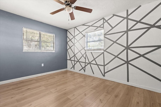 spare room featuring a ceiling fan, light wood-style floors, baseboards, and an accent wall