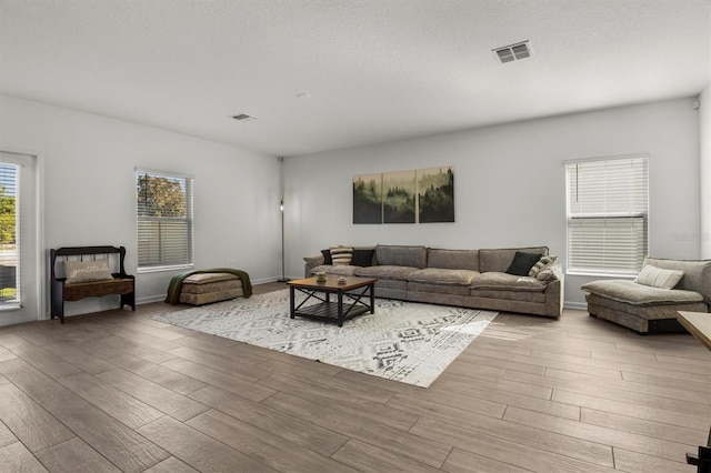 living room with visible vents, a textured ceiling, baseboards, and wood finished floors