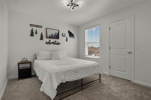 carpeted bedroom featuring a notable chandelier and baseboards