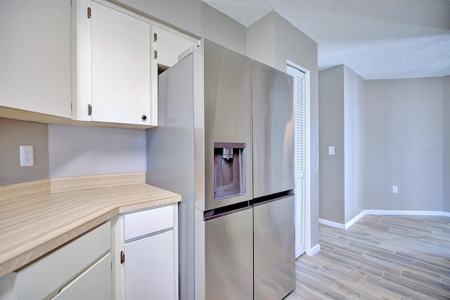 kitchen featuring stainless steel fridge with ice dispenser, light wood-type flooring, light countertops, white cabinets, and a textured ceiling