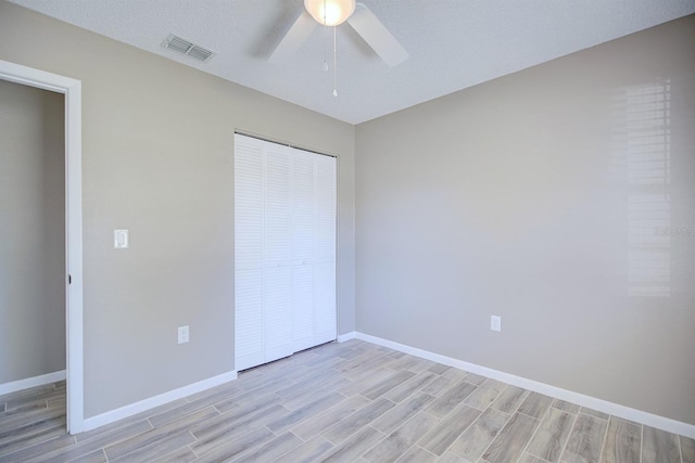 unfurnished bedroom with wood finish floors, visible vents, a closet, baseboards, and ceiling fan