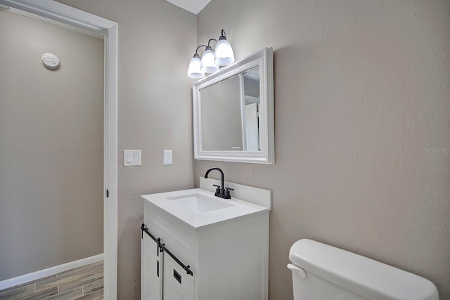 bathroom with baseboards, toilet, wood finished floors, and vanity