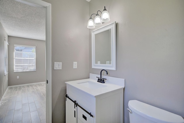 half bathroom with baseboards, toilet, vanity, wood finished floors, and a textured ceiling