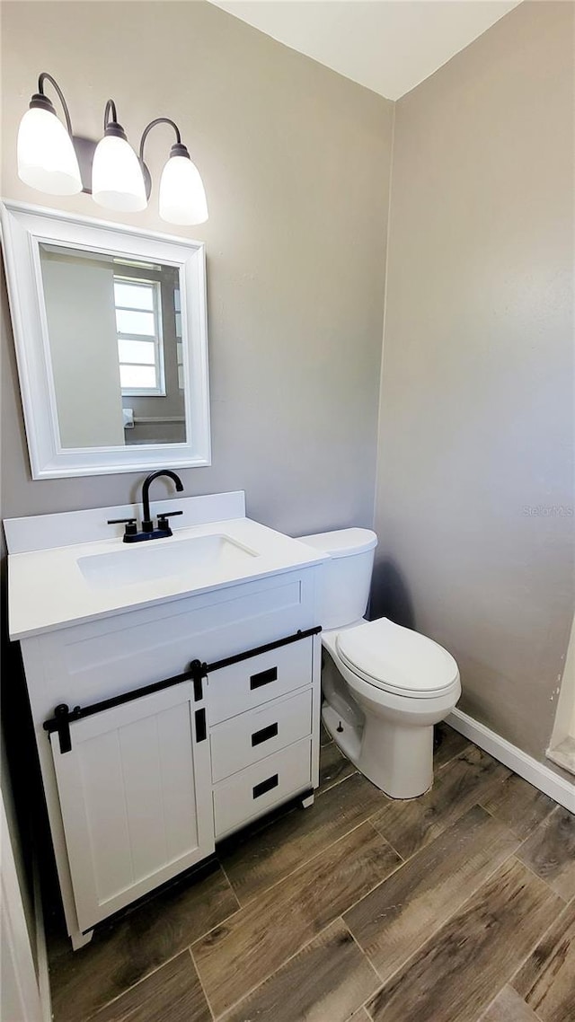 half bath with toilet, wood finished floors, and vanity