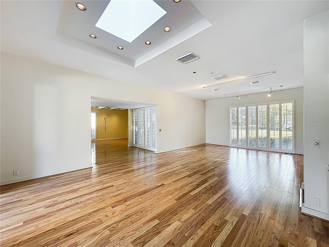 spare room featuring a tray ceiling, a skylight, wood finished floors, and visible vents