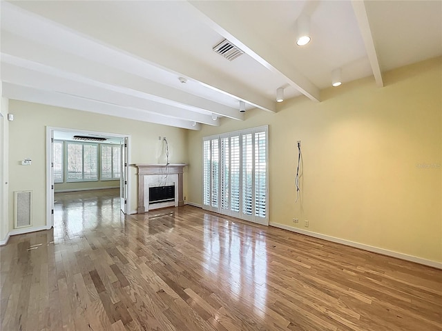 unfurnished living room with visible vents, baseboards, beamed ceiling, a fireplace, and wood finished floors