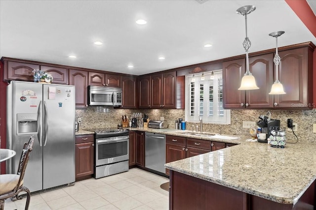 kitchen featuring tasteful backsplash, light stone counters, a peninsula, stainless steel appliances, and a sink