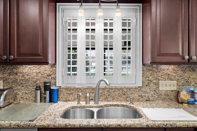 details featuring dark brown cabinets, backsplash, light stone counters, hanging light fixtures, and a sink