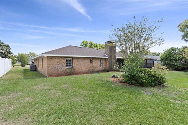 back of property featuring brick siding, central air condition unit, a lawn, and a chimney