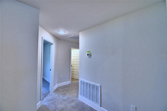 hallway with baseboards, visible vents, and light tile patterned floors