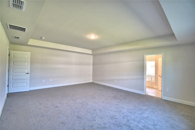 spare room with a tray ceiling, visible vents, and carpet